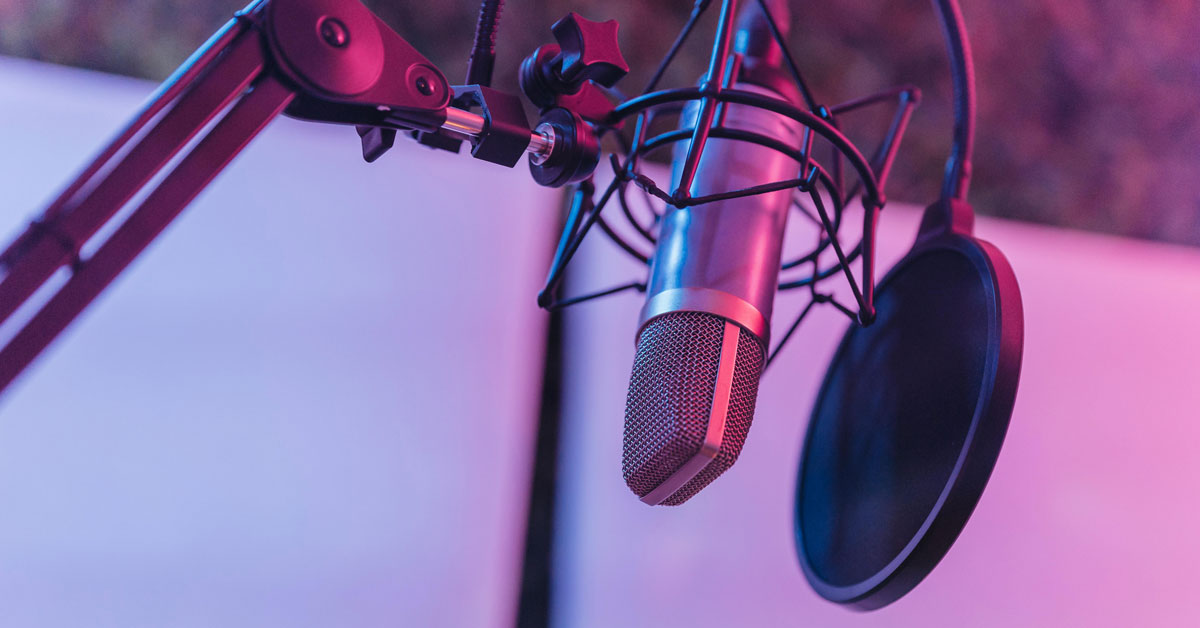 A podcast microphone hangs from a stand, with pink and blue lighting in the background