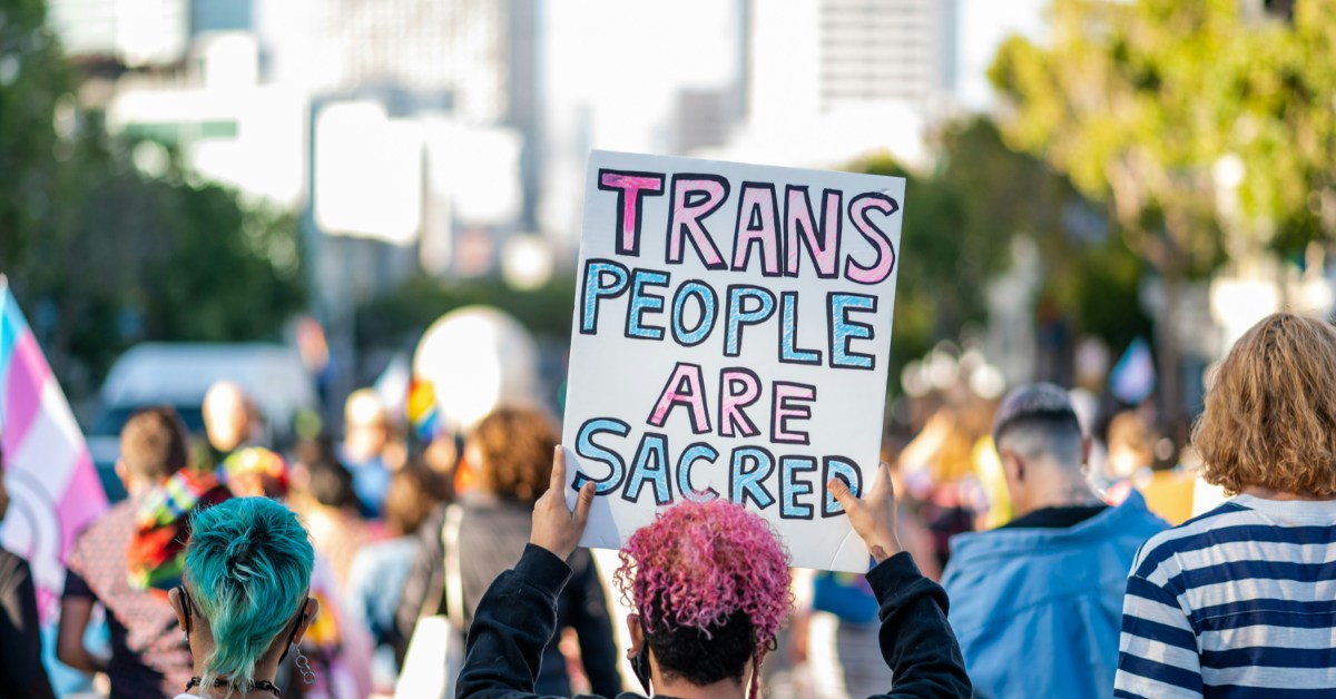A protester holds up a sign that reads "trans people are sacred"