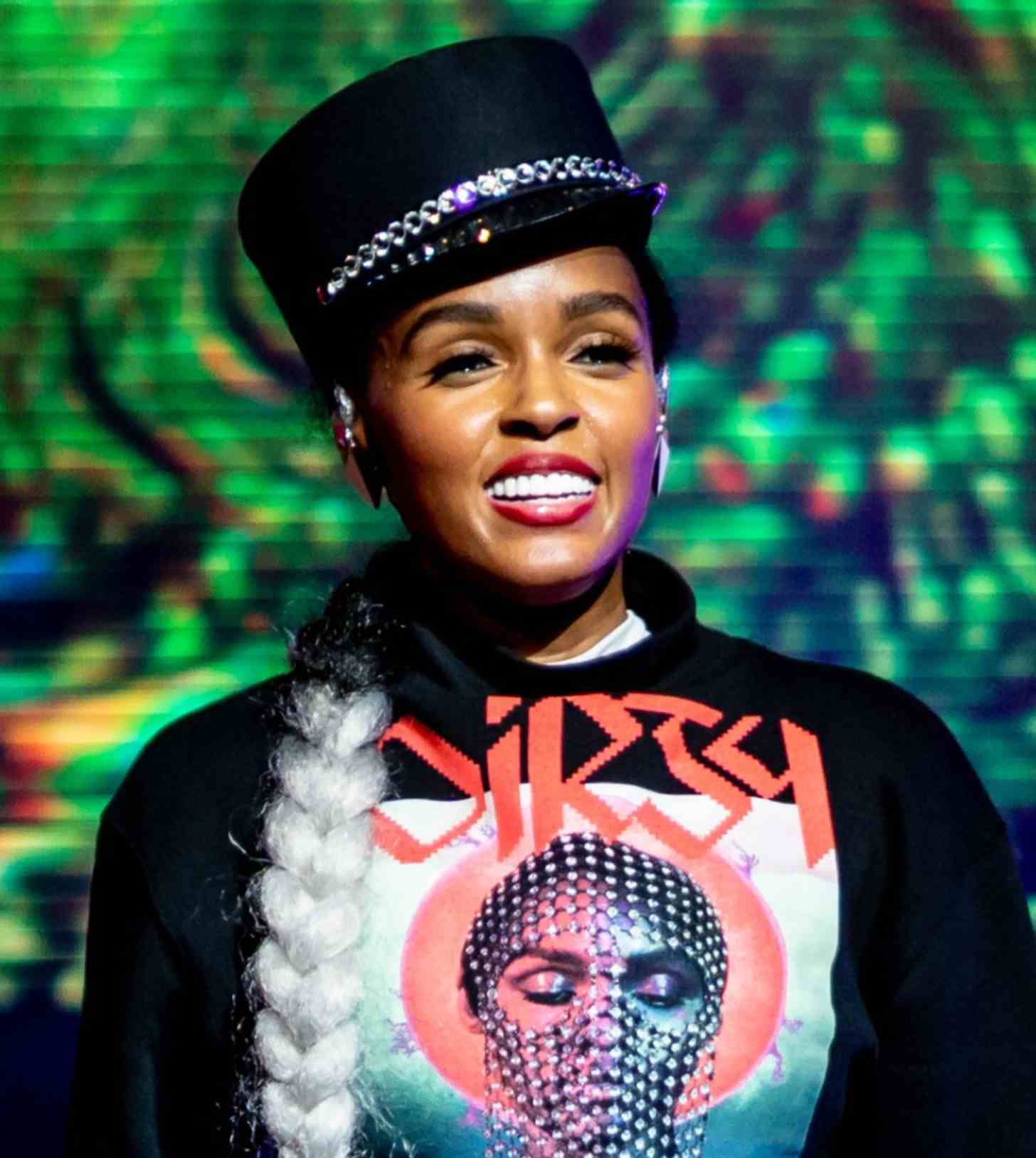 Janelle Monae stands in front of an LED screen at a music concert, smiling