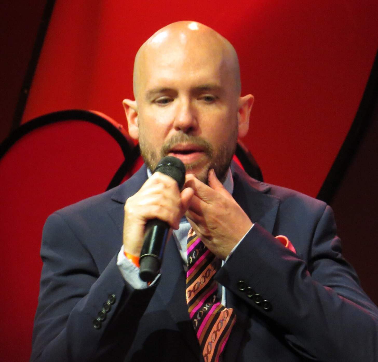 British comedian Tom Allen speaks into a mic at a stand up comedy club