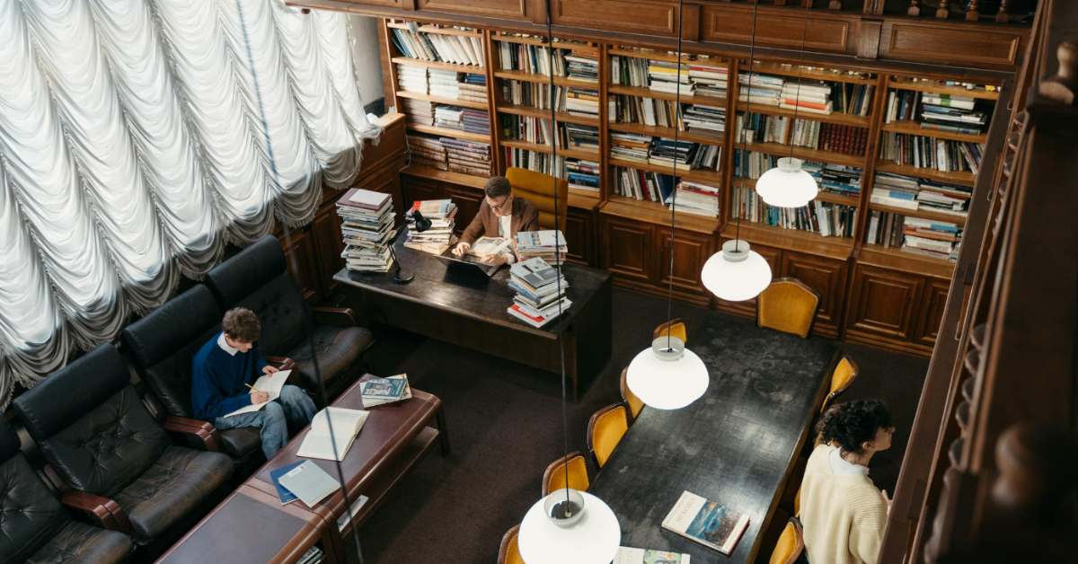 A picture of a library, taken from a second story looking down. Three different people are milling about