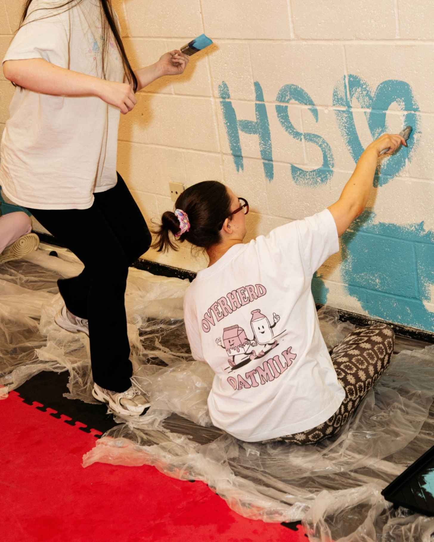 Two girls paint a white brick wall
