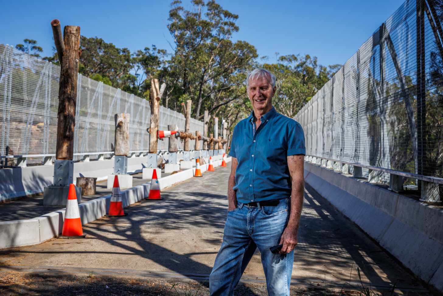 A man in blue jeans and a blue shirt stands on a bridge in Australia