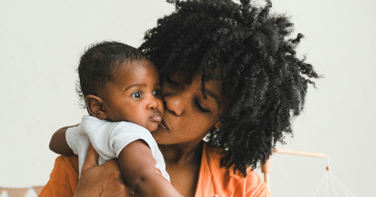 A Black mother kisses her baby on the cheek 