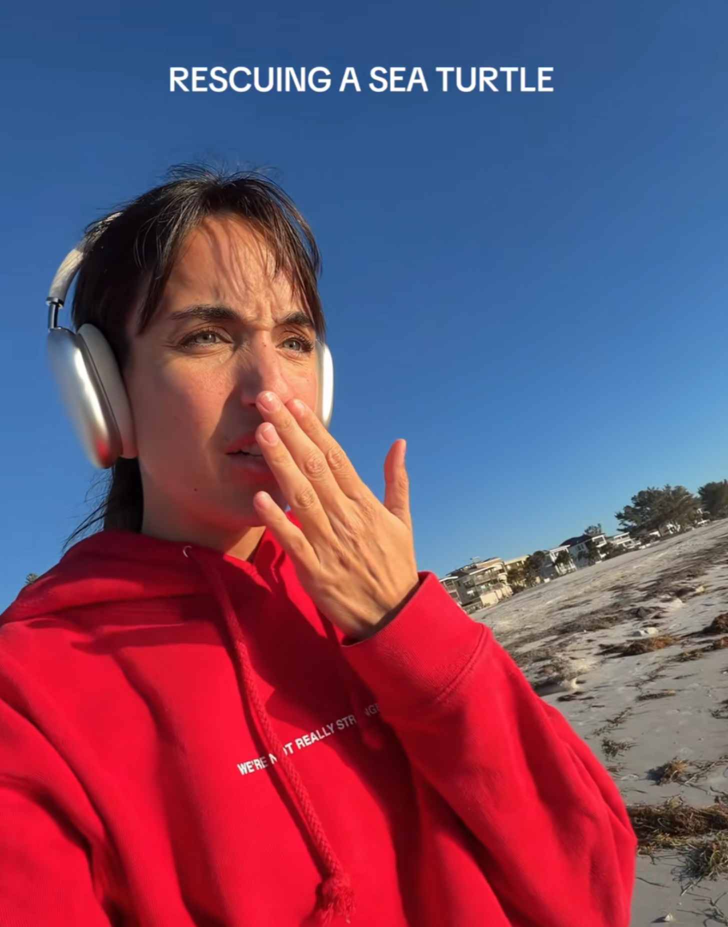 A woman in a red hoodie gasps as she looks offscreen. She is on a beach during the day. The text says: RESCUING A SEA TURTLE