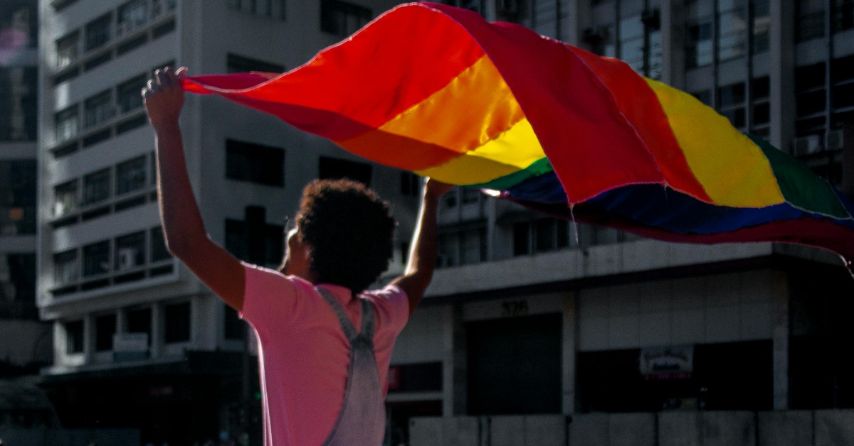 A person holds a pride flag over their head as they walk down a city street