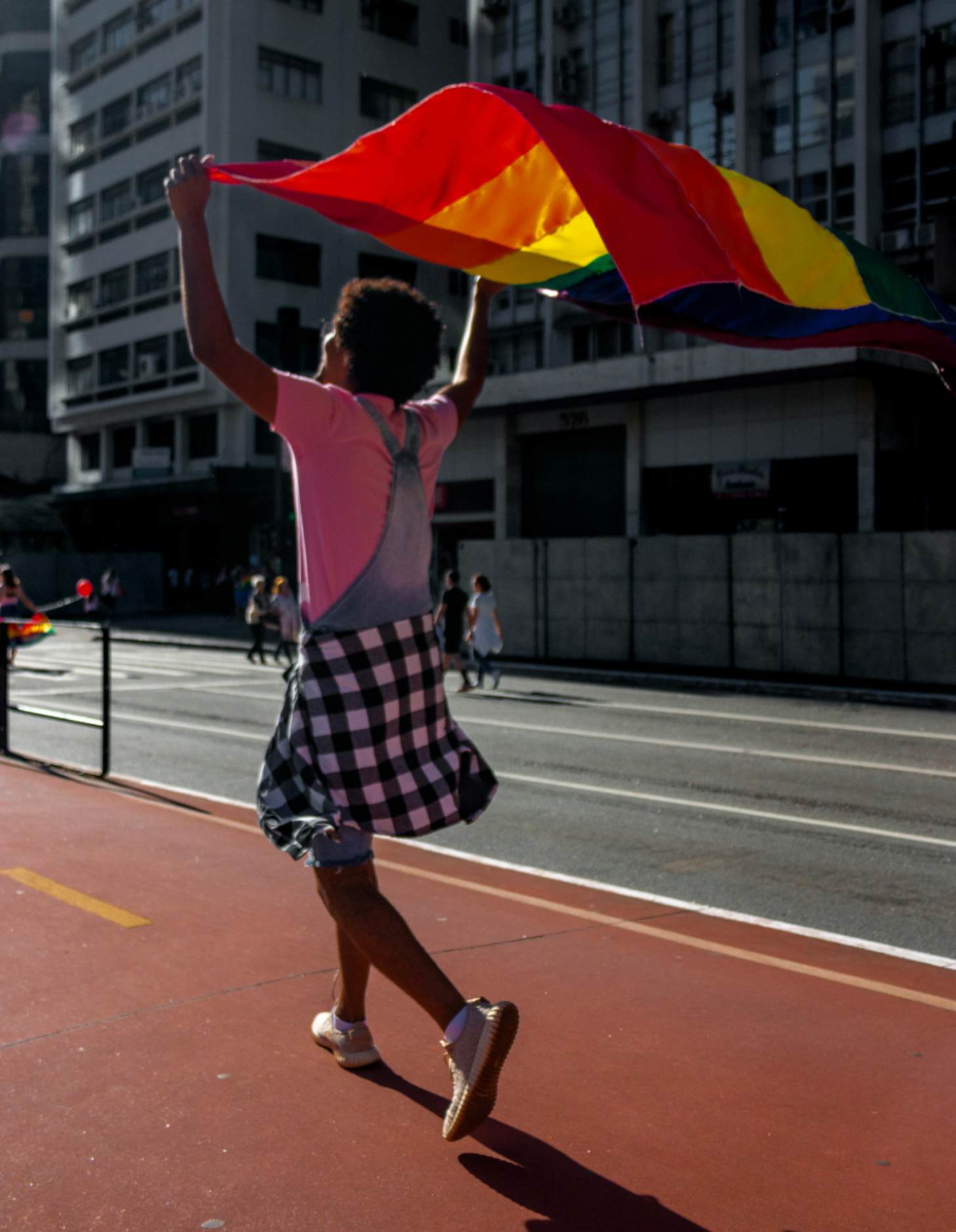 A person holds a pride flag over their head as they walk down a city street