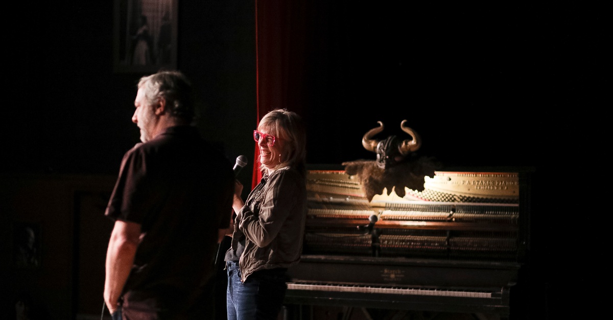 Maria Bamford and Judd Apatow stand on stage in a comedy club