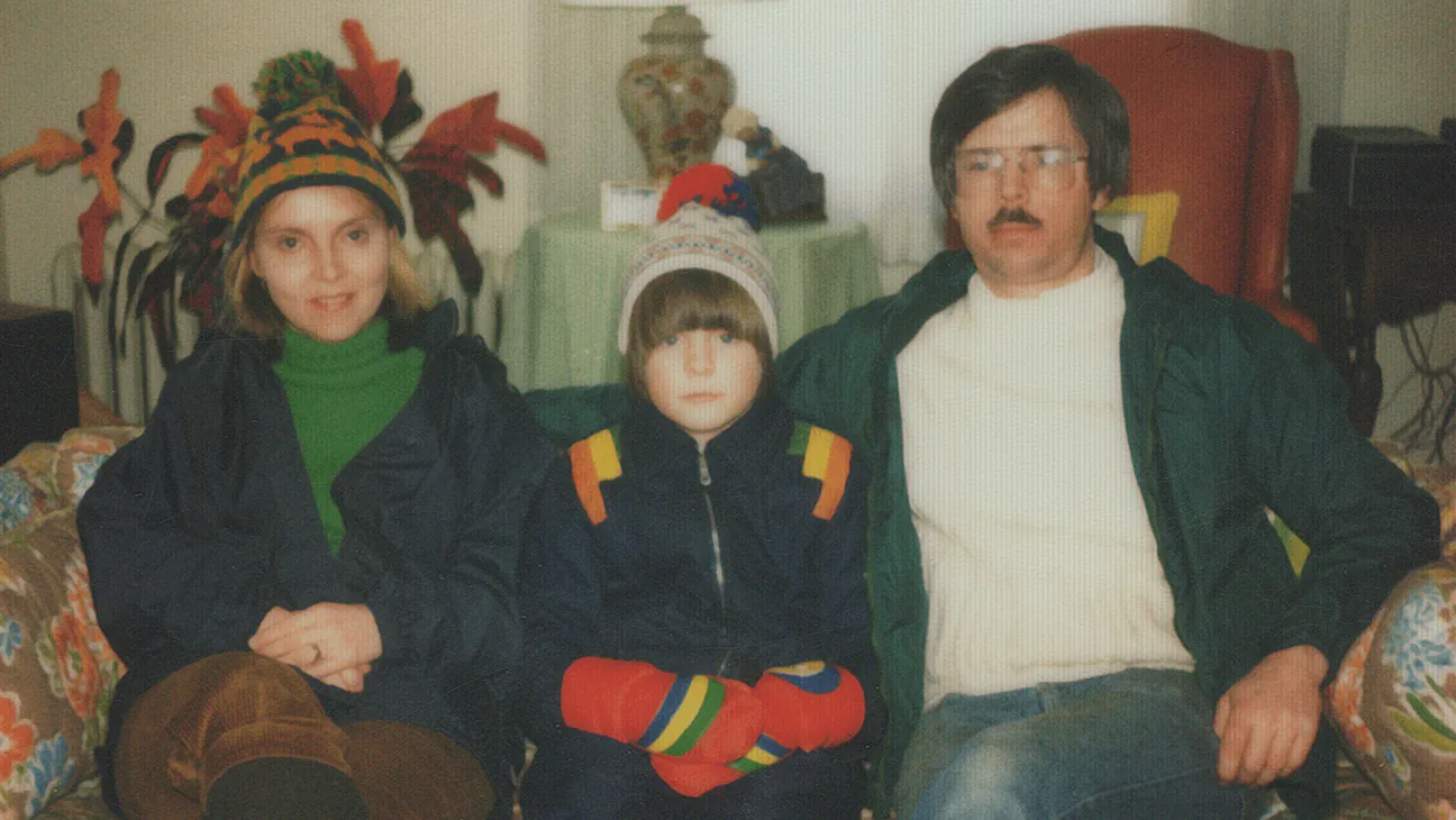 A mother, daughter, and father sit on a couch in a vintage picture from the 1960s.