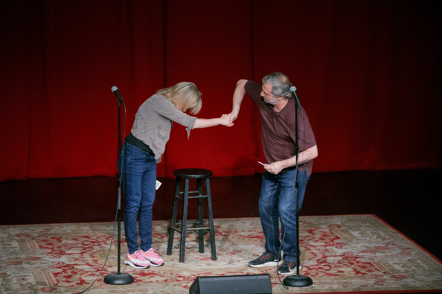 Maria Bamford and Judd Apatow shake hands on stage in an awkawrd bowing manner.
