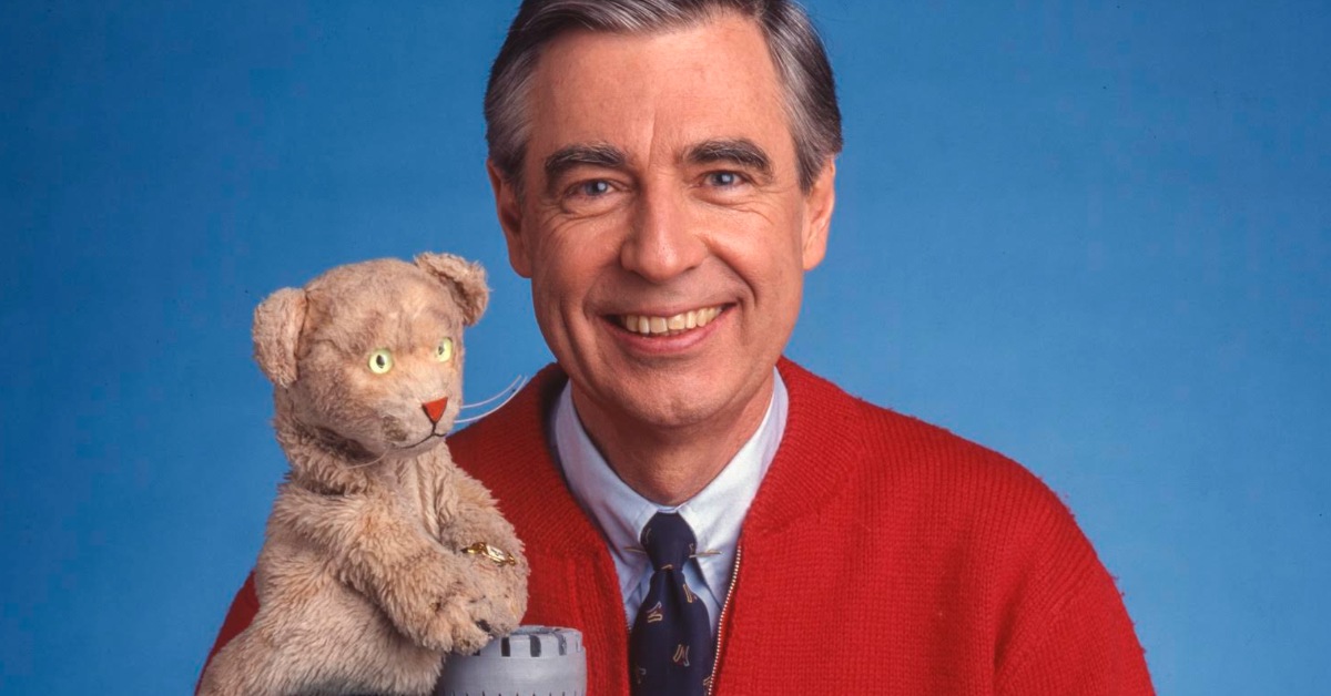 Mister Rogers, in his iconic red cardigan, holds up Daniel from Mister Rogers Neighborhood.