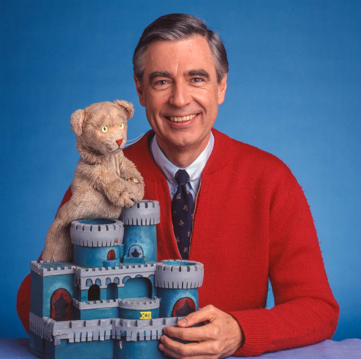 Mister Rogers, in his iconic red cardigan, holds up Daniel from Mister Rogers Neighborhood.