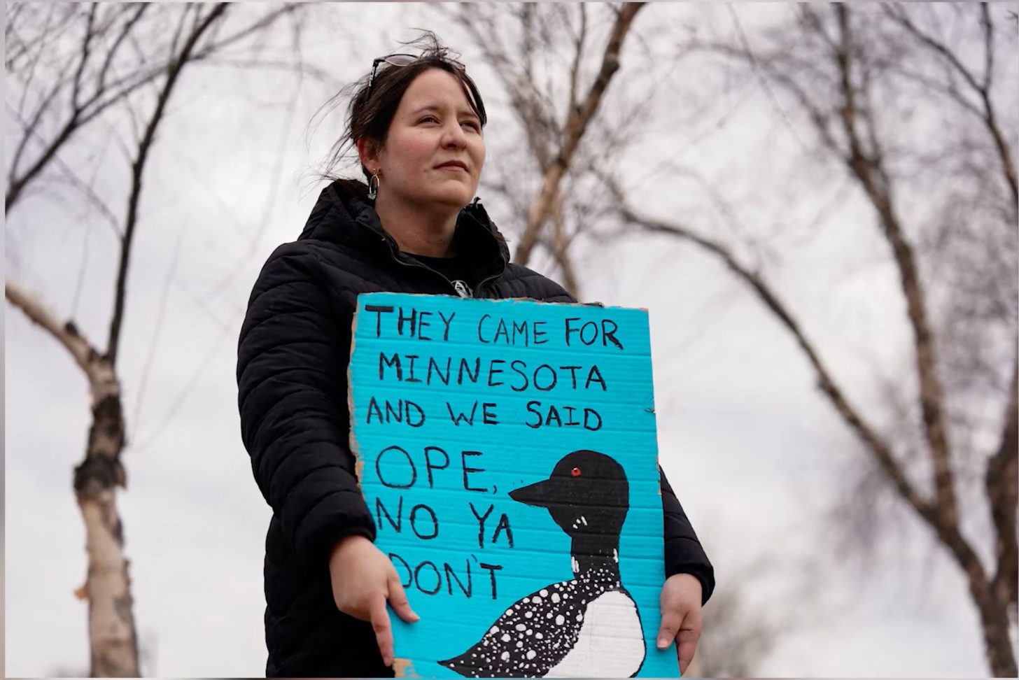 A protestor holds up a blue sign that reads: They came for Minnesota and we said Ope, No Ya Don't