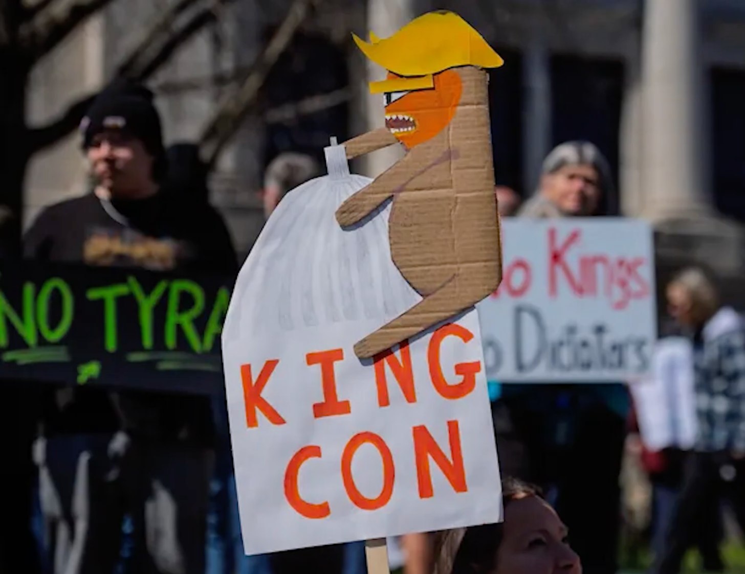 A crude cardboard version of Trump as King Kong climbing a building. The sign reads "King Con."