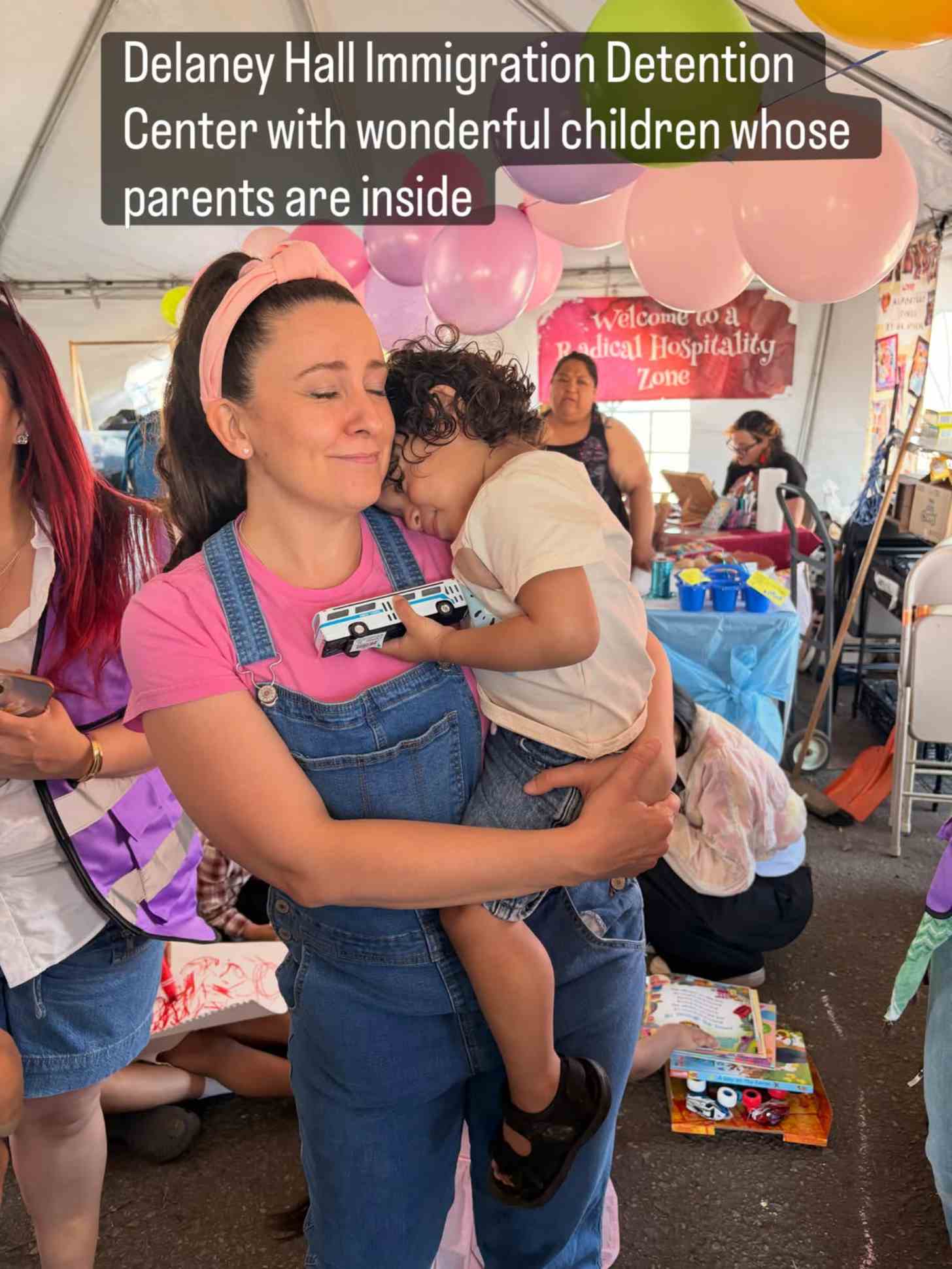 Children's entertainer Ms. Rachel wears her signature pink headband, pink t-shirt, and denim overalls, while hugging a child outside of Delaney Hall Detention Center