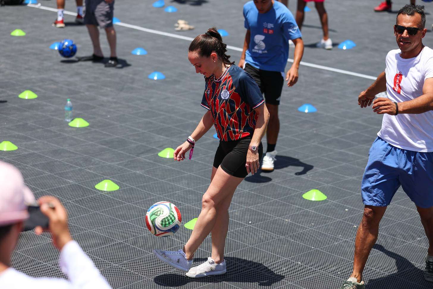 A female athlete, surrounded by other athletes, juggles a soccer ball