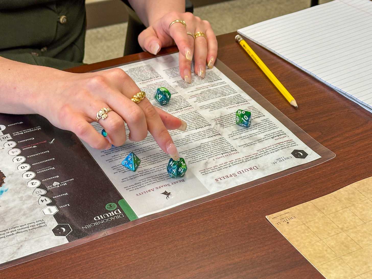 A close-up of a person's hands rolling a green and blue die in a game of Dungeons & Dragons