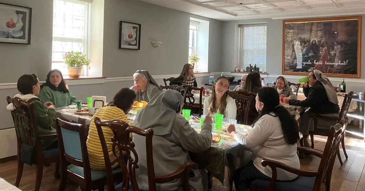 Young women sit around a dining table with nuns