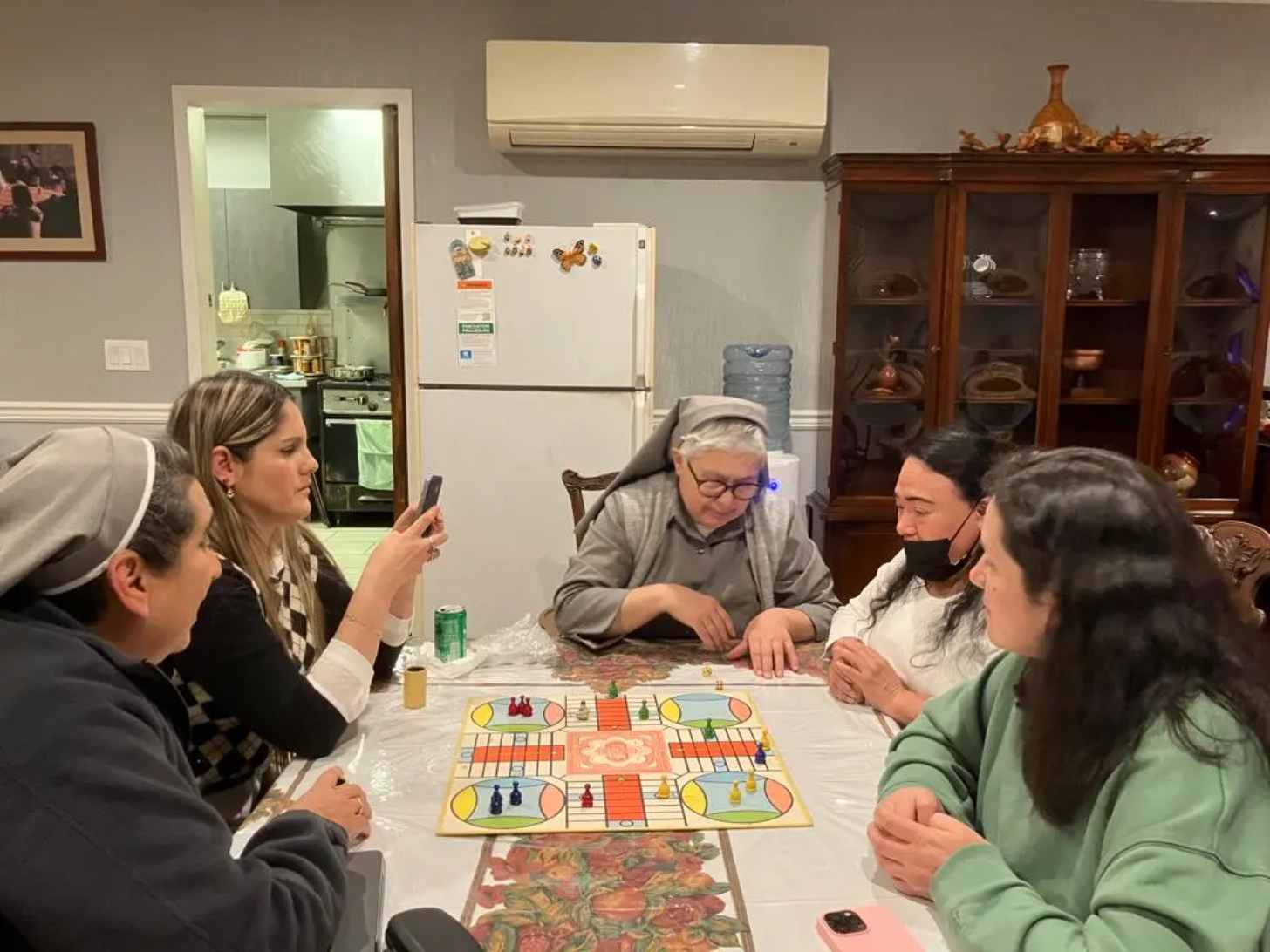 Young women play games around a table with two nuns