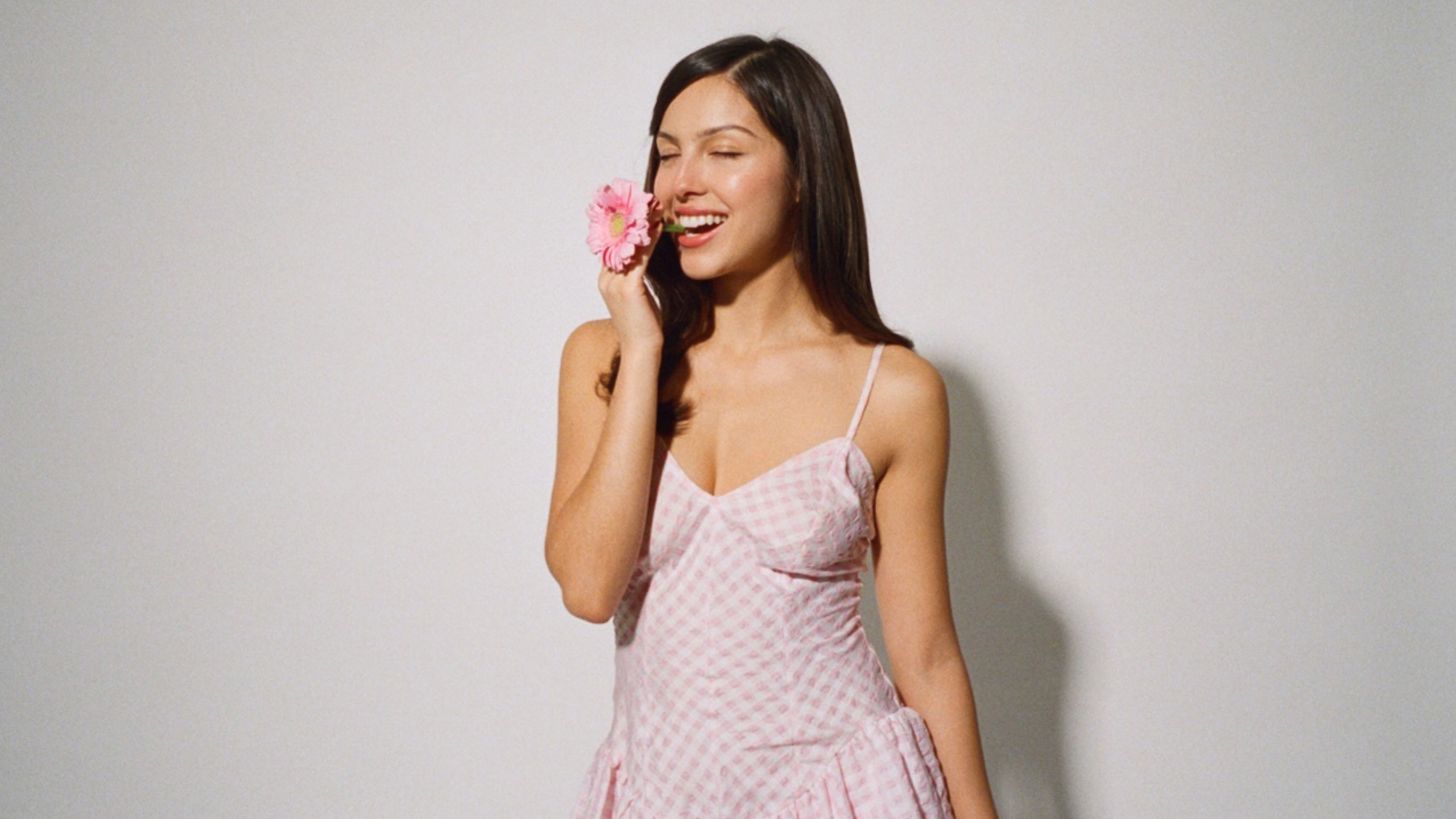 Olivia Rodrigo holds a pink daisy near her mouth
