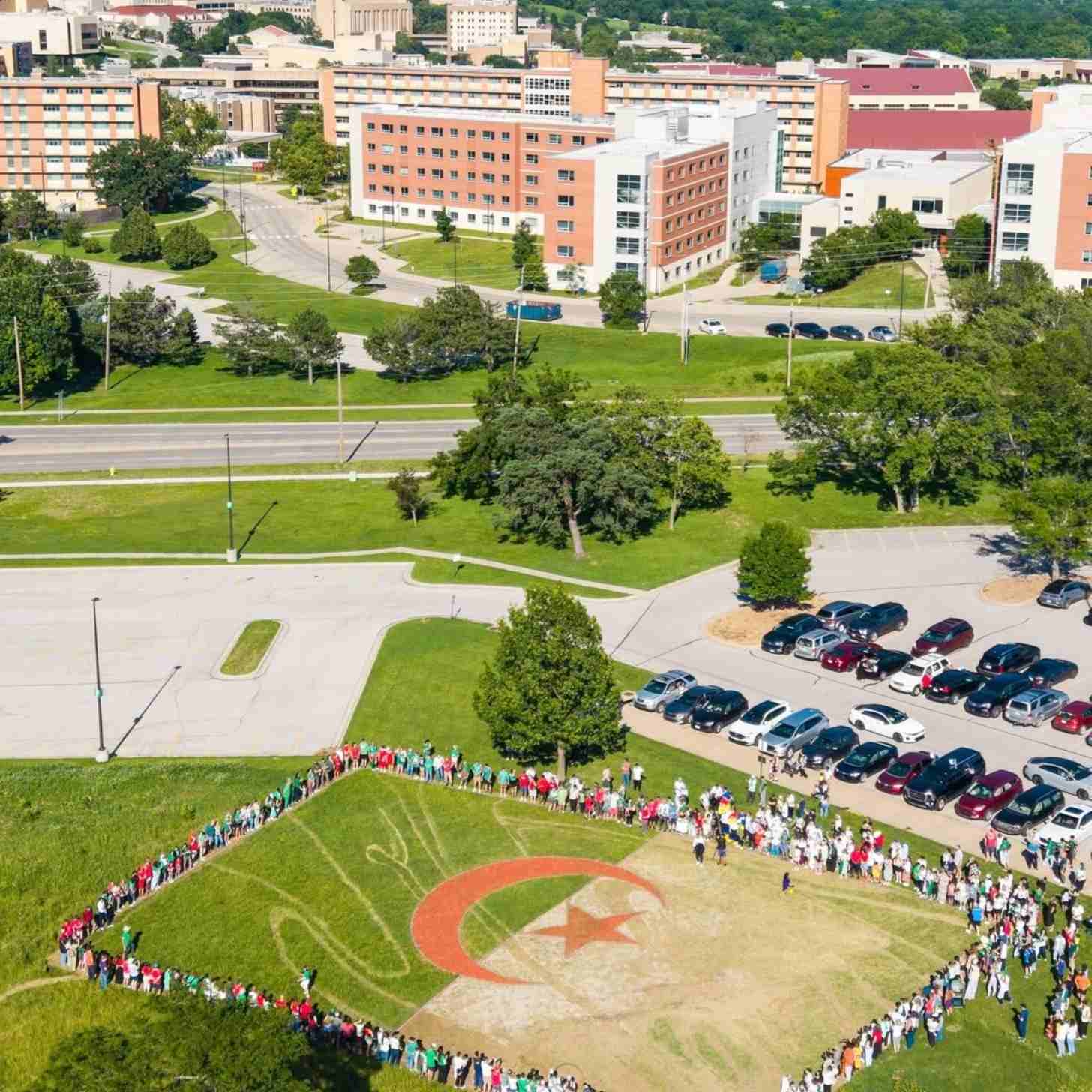 An aerial view of a university campus where a large crowd forms a human outline around a field painted as the Algerian flag, green and white with a red crescent and star.