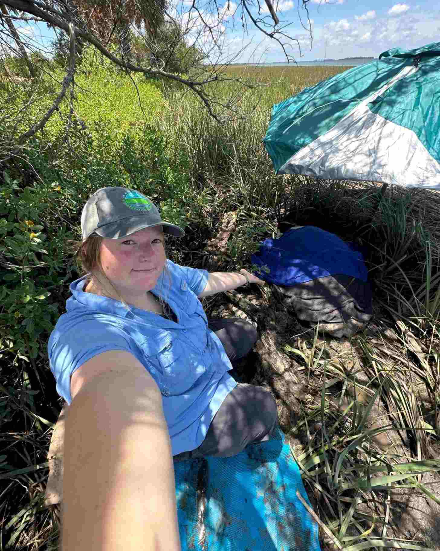 A woman takes a selfie with a turtle under a beach umbrella