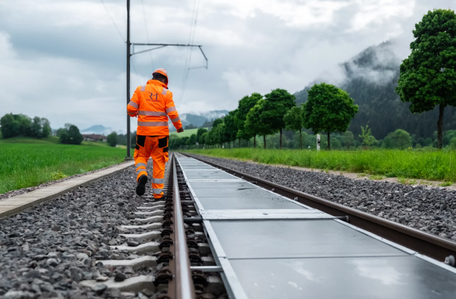 A railway worker in bright orange safety gear inspects solar panels on train tracks