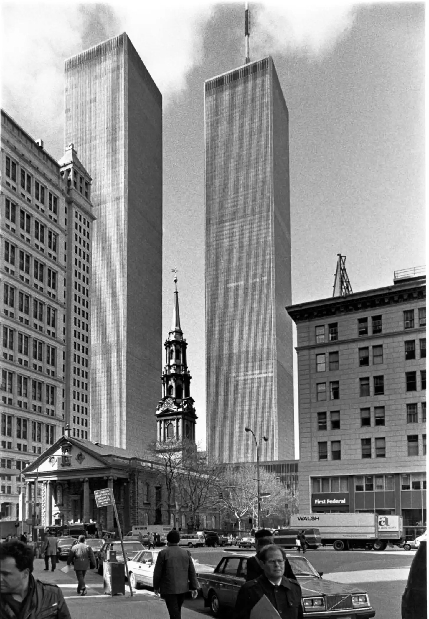 Two tall rectangular office towers rise behind a historic church with a steeple in an urban street scene with pedestrians, parked cars, and a delivery truck marked "Walsh" and "First Federal."