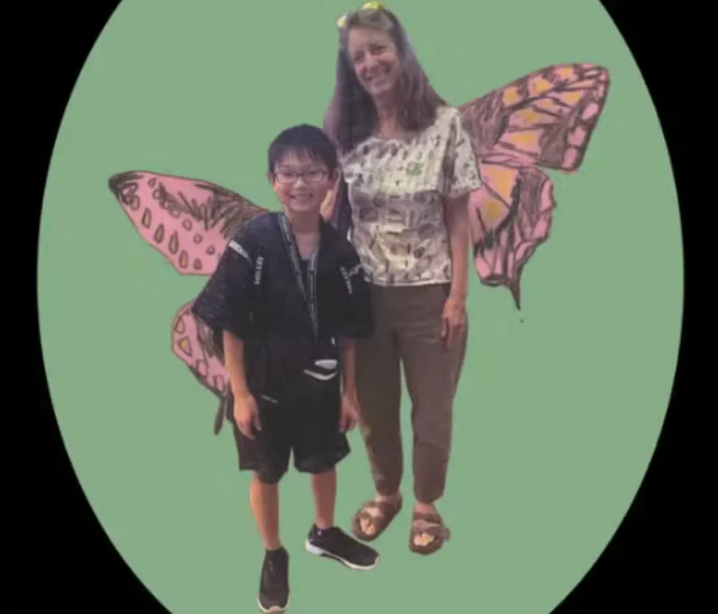 An adult and child stand together against a green background, both wearing illustrated pink butterfly wings digitally added to the image.