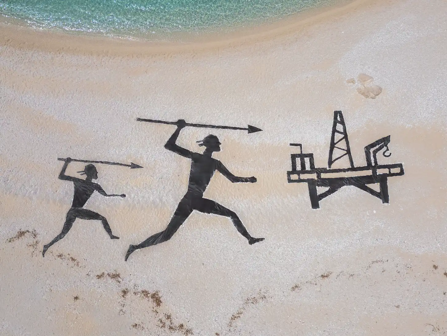Black silhouette figures drawn on wet sand at a beach shore, showing two people in running poses holding spears pointing right, and an oil derrick structure on the right.