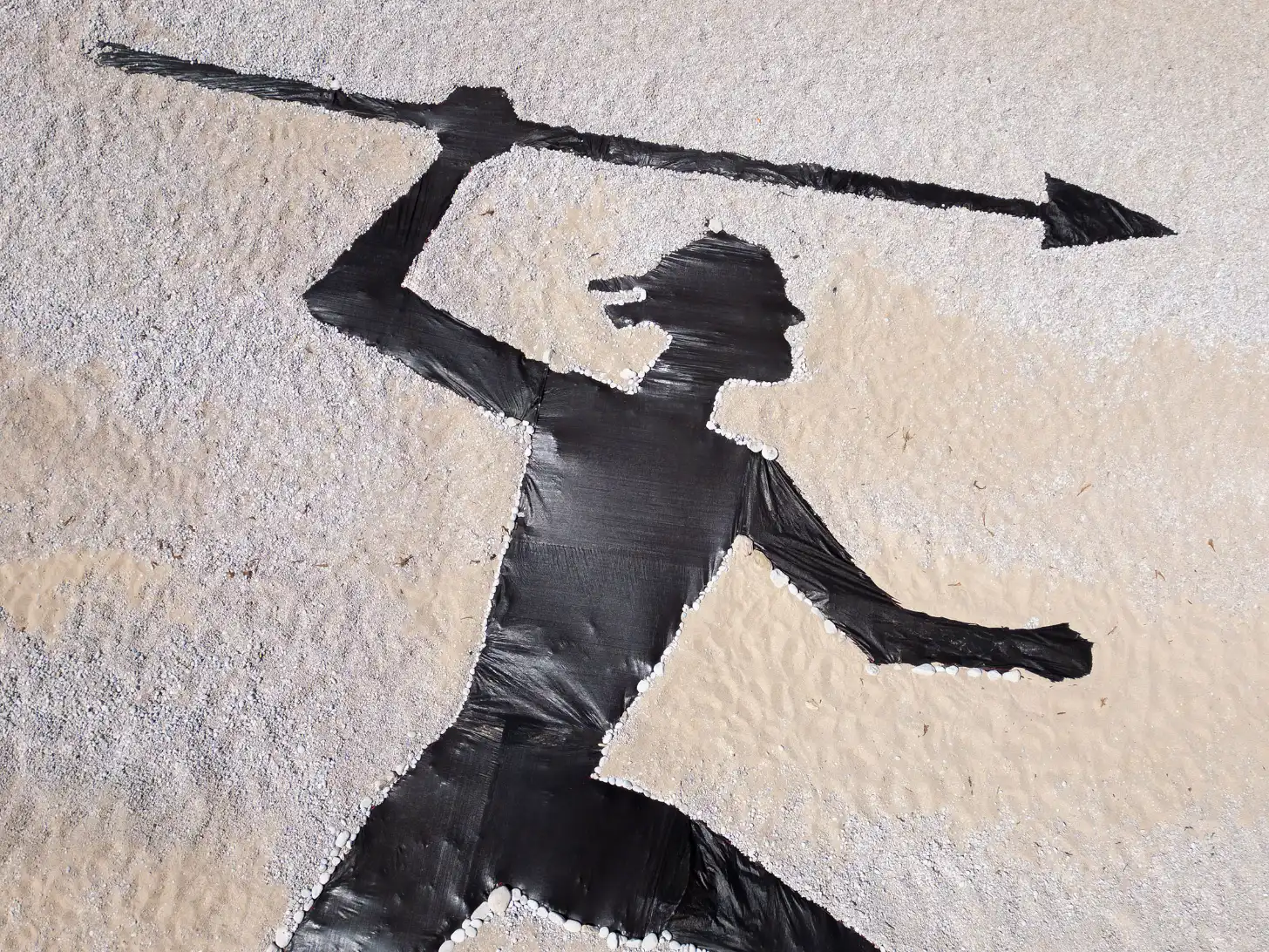 Black silhouette of a figure with an arrow displayed on a sand surface.