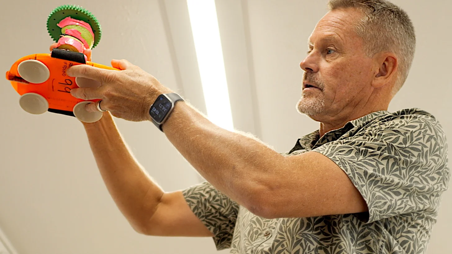 Man in a patterned shirt holding an orange drone sensor with colorful stacked rings.