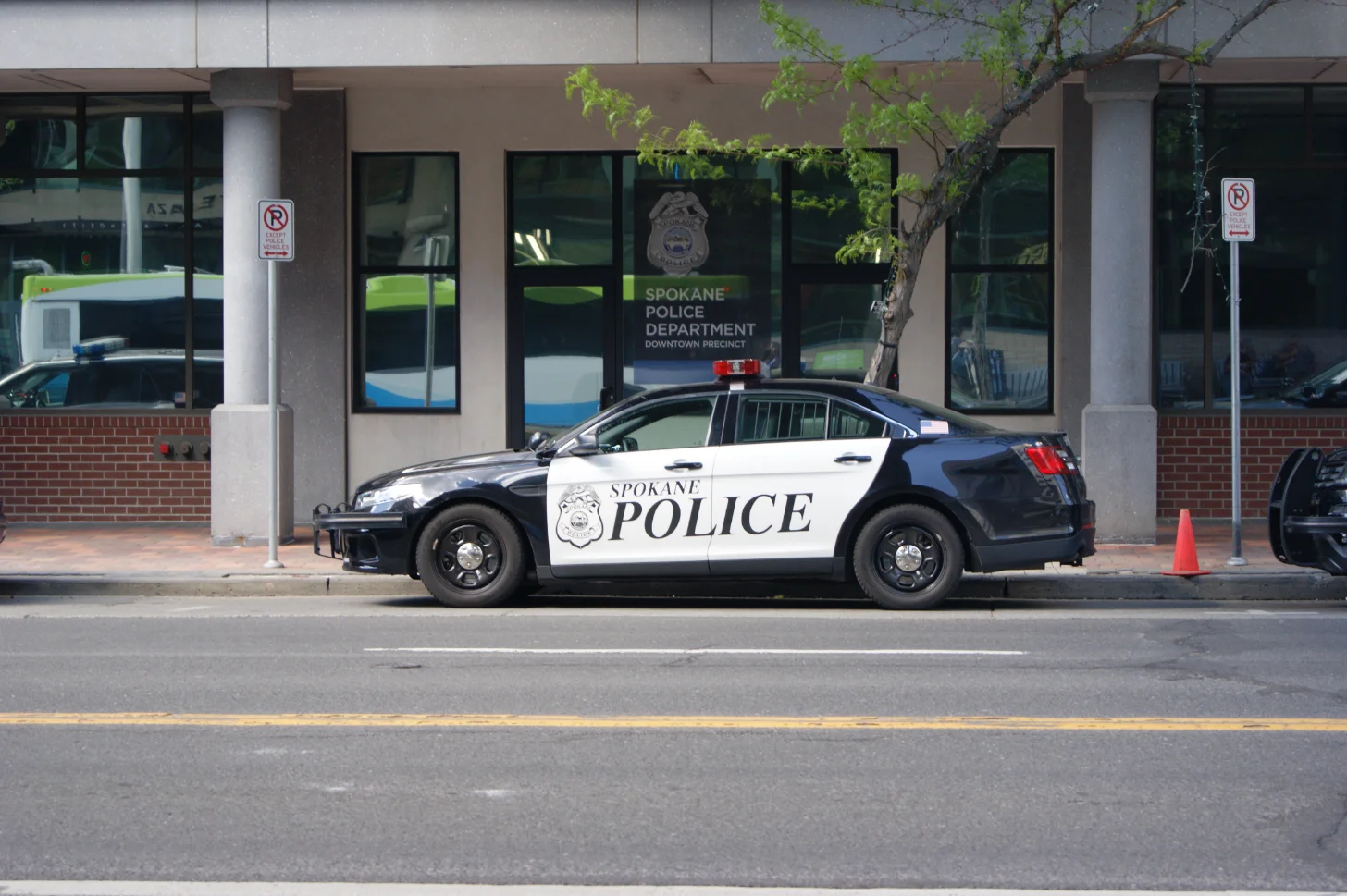 A Spokane Police Department patrol car parked in front of the Downtown Precinct building. The vehicle is black and white with "SPOKANE POLICE" text and a badge visible on its side.