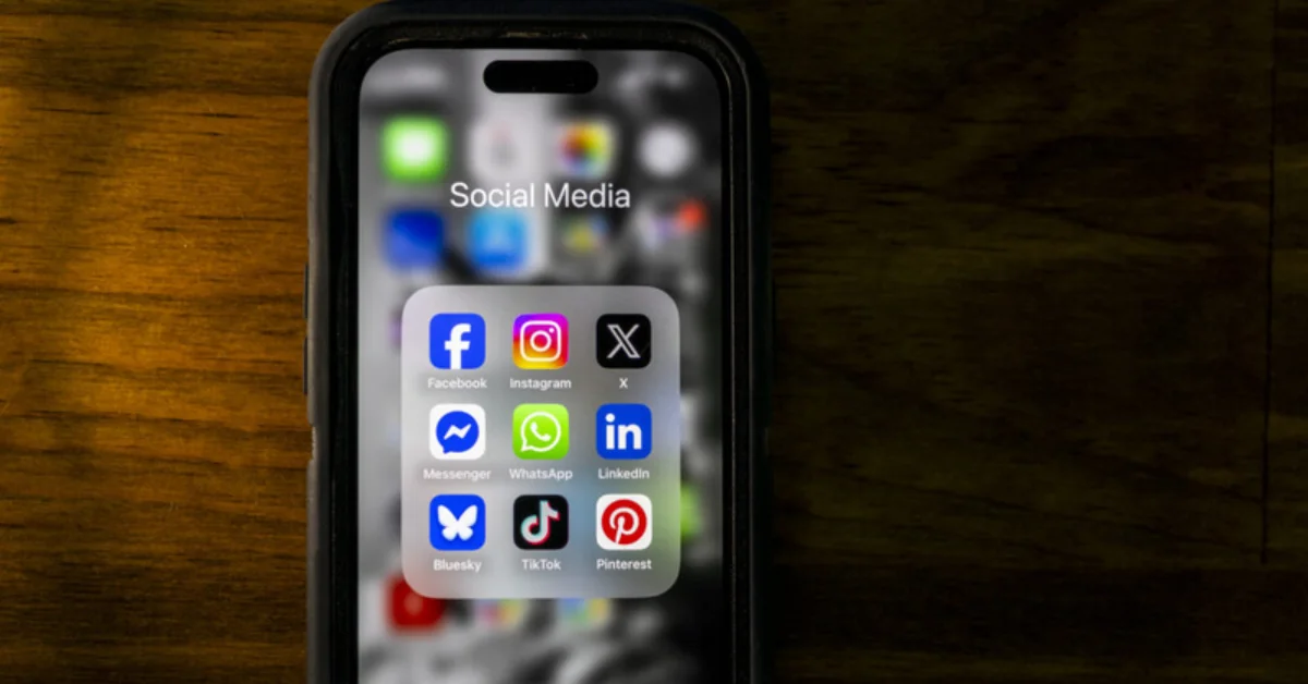 iPhone displaying a "Social Media" folder with nine app icons: Facebook, Instagram, X, Messenger, WhatsApp, LinkedIn, Bluesky, TikTok, and Pinterest.