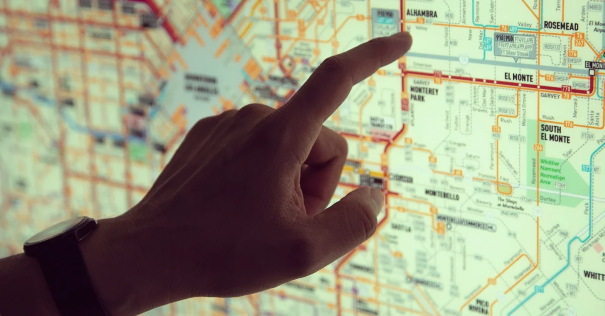 A person's hand points to a detailed street map showing areas including El Monte, Rosemead, and South El Monte, with roads marked in red and orange lines and various neighborhoods outlined in green.