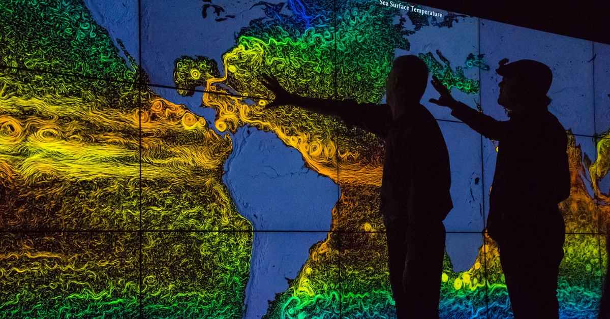 Two people look at a large map of sea surface temperatures on a screen