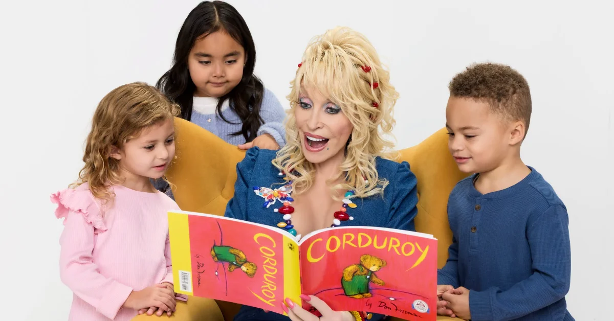 A woman with blonde curled hair wearing a denim jacket reads a book titled "Corduroy" to four children seated around her against a white background.