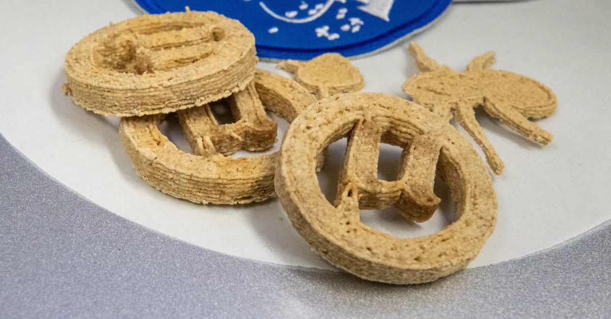 Three tan-colored pastries with hollow centers arranged on a white plate, with a blue container visible in the background.