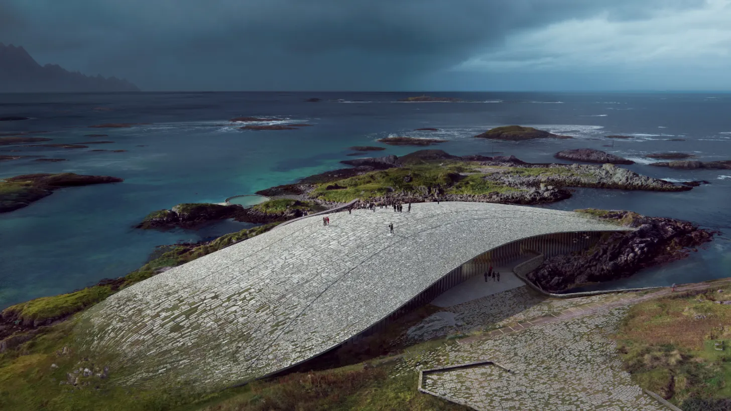 A modern curved building with a ribbed exterior sits on a rocky coastal island surrounded by turquoise water and smaller islands under an overcast sky. Several visitors walk on the building's top surface and nearby terrain.