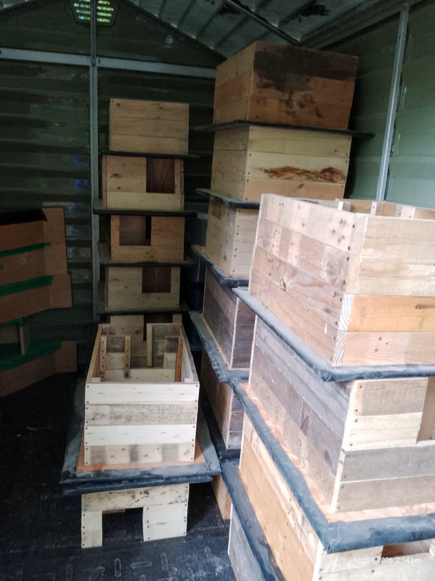 Wooden crates and boxes of varying sizes stacked inside a large truck or cargo container, with metal shelving visible on the left side.