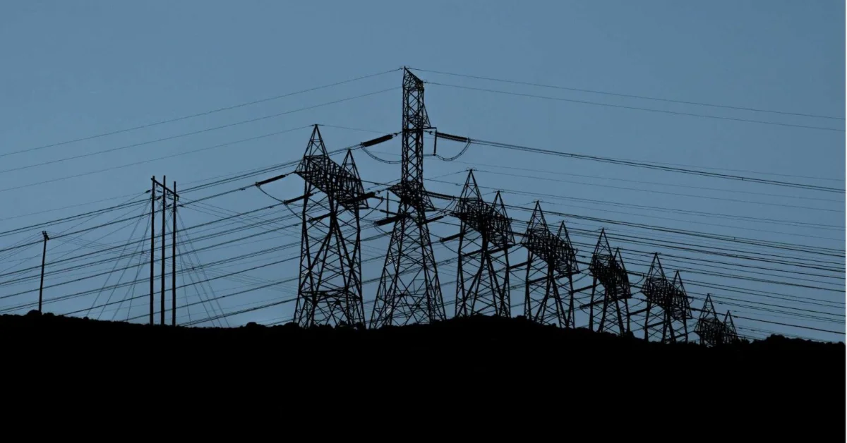 Silhouetted electrical transmission towers and power lines against a blue sky at dusk or dawn.