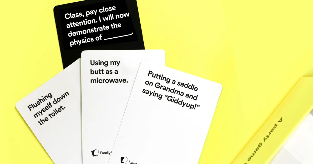 Cards spread on a yellow background. Visible text includes: "Class, pay close attention. I will now demonstrate the physics of ____." on a black card; "Using my butt as a microwave," "Flushing myself down the toilet," and "Putting a saddle on Grandma and saying 'Giddyup!'" on white cards.