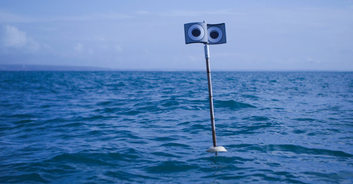 A pole mounted with two circular speakers extends from the ocean surface against a blue sky and calm sea.