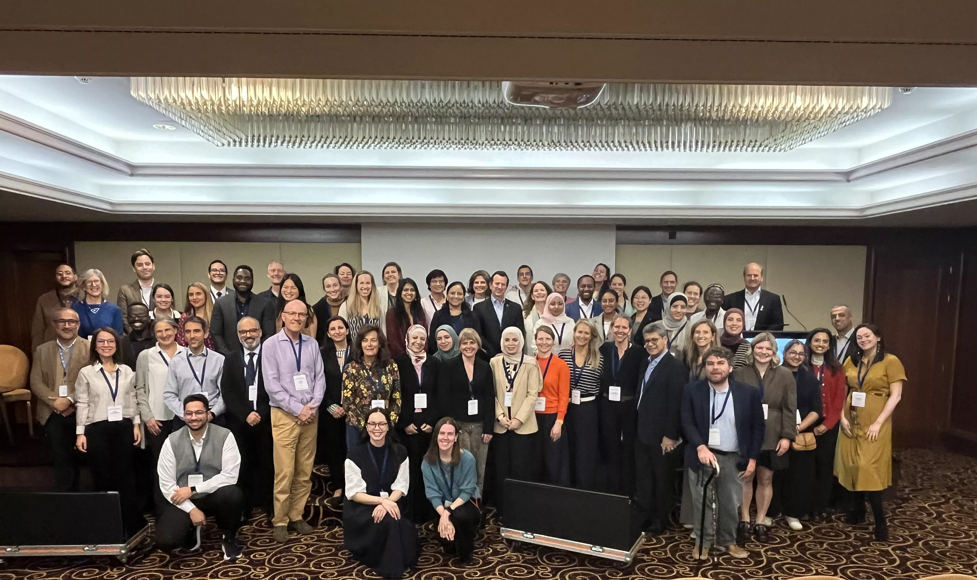 Large group of diverse people posing for a photo in a conference room with a projector screen behind them.