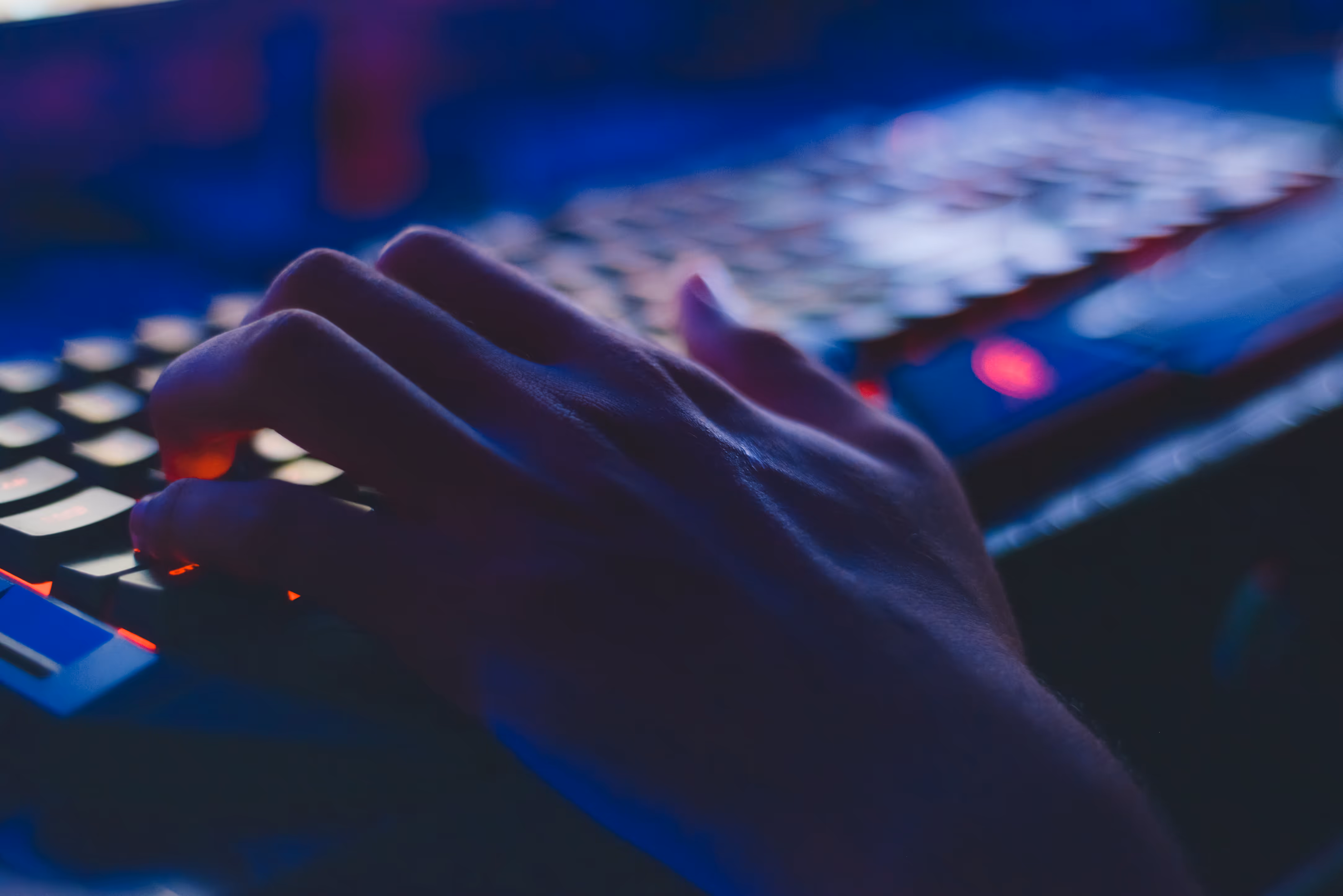 Hand på bakgrundsbelyst tangentbord i mörk miljö, symboliserar programmering, gaming och digitalt arbete.