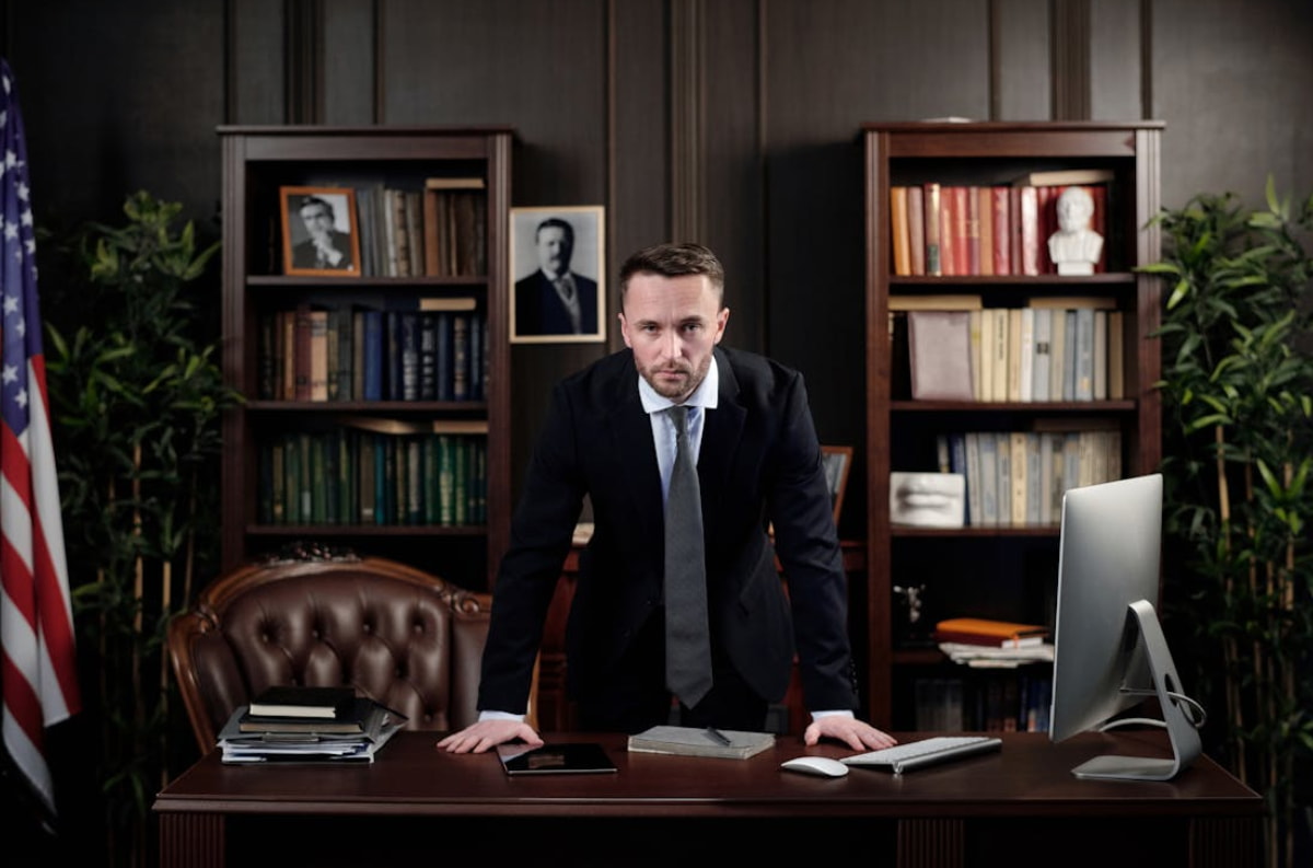 A man in a suit and tie seated at a desk, focused on his work with a professional demeanor.  