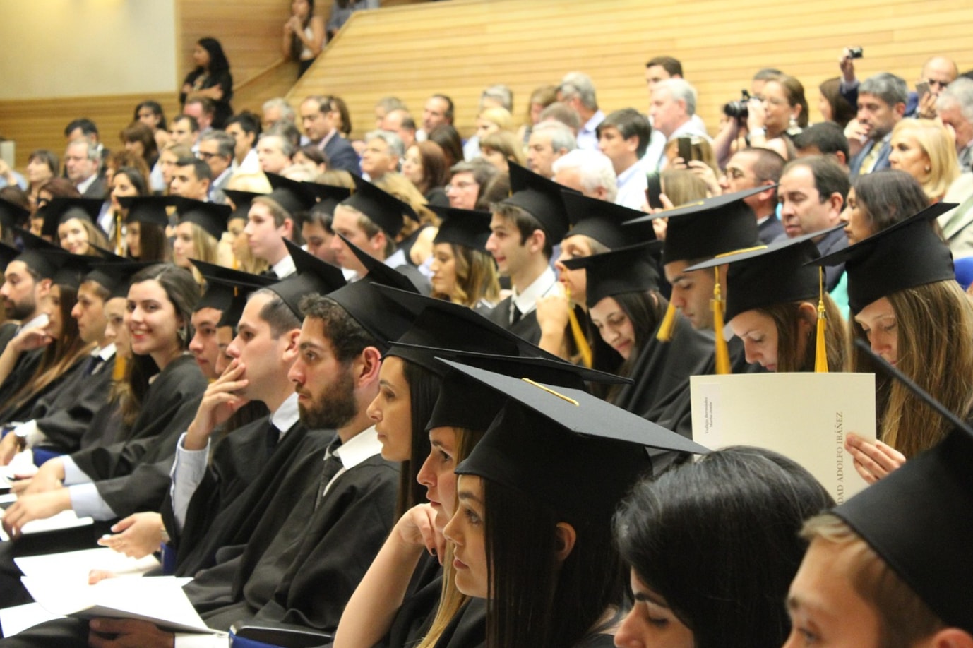 A large group of graduates seated in a spacious auditorium, celebrating their academic achievements together