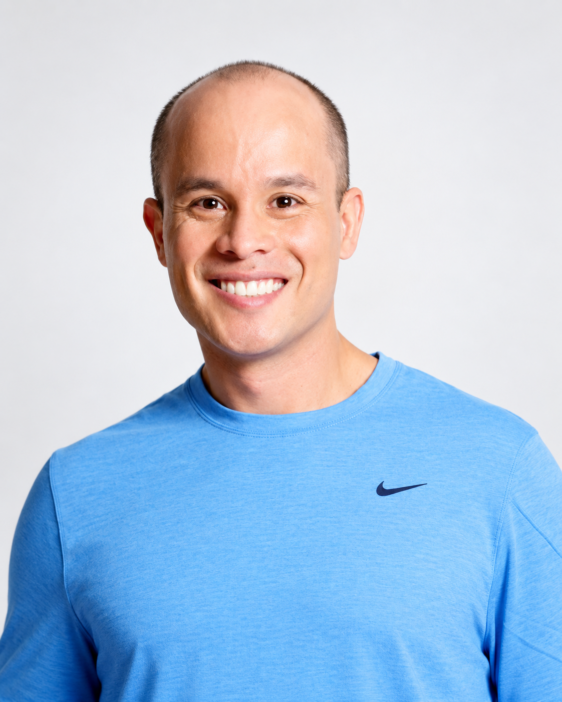Smiling man wearing a light blue Nike shirt against a white background.
