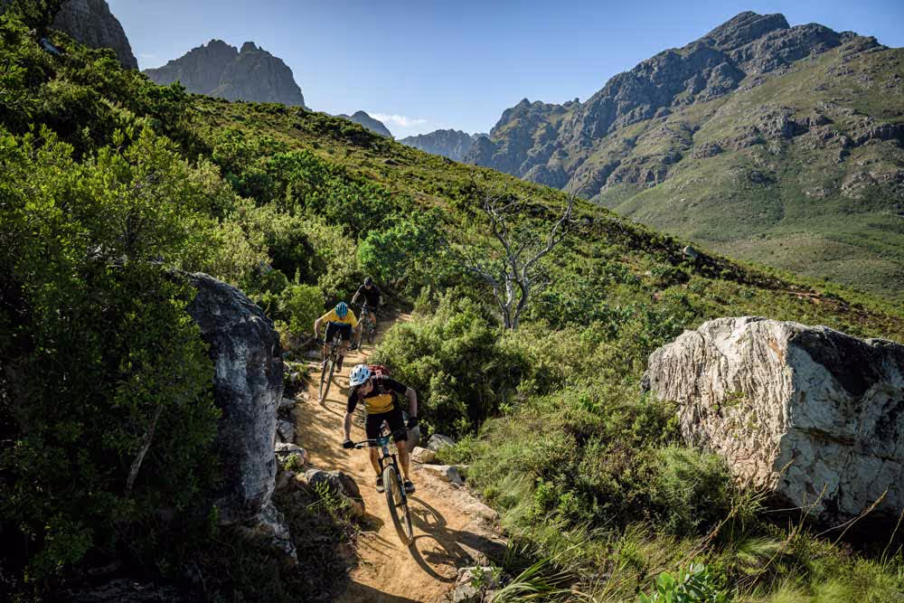 Mountain bikers riding trail through rocky landscape with lush green mountains