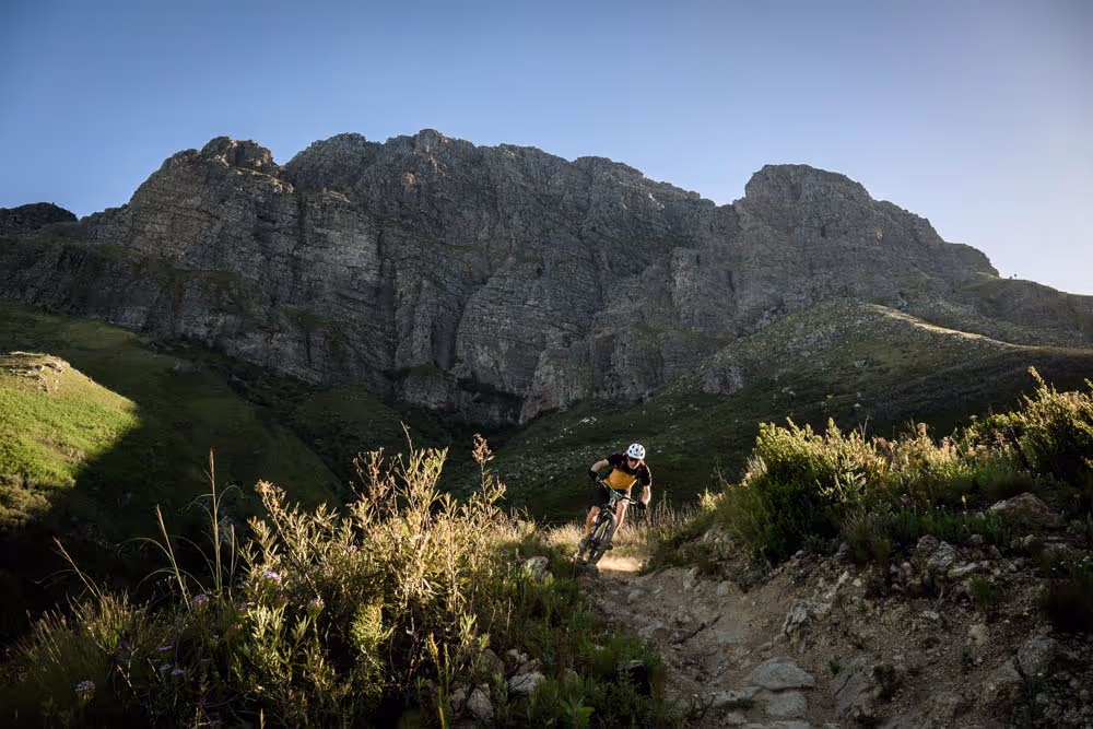 Mountain biker riding trail with rocky mountain backdrop at golden hour